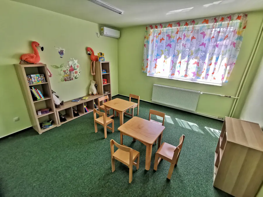Sală de grupă cu bibliotecă joasă și masă de lucru