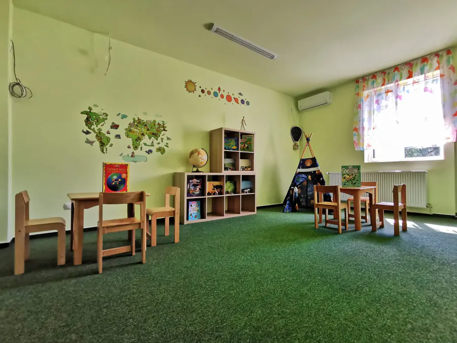 Sală de grupă cu plante, rafturi joase și mese de lucru